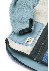 Ζακέτα από φλις σε ανοιχτό μπλε και κρεμ αποχρώσεις, με φερμουάρ, τσέπη και ετικέτα. Μαλακή υφή με διάφορα πάνελ υφάσματος.