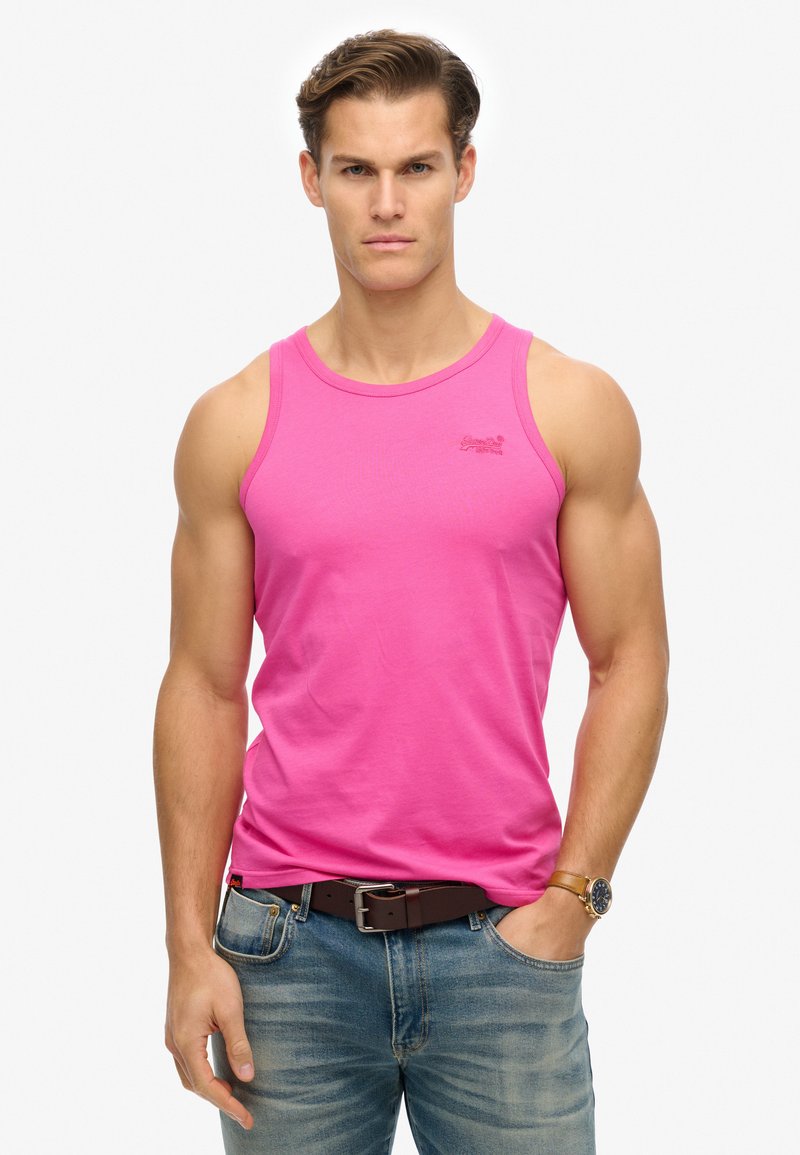 Top de tirantes ajustado de algodón rosa con correas anchas, escote reforzado y pequeño logo. Combinado con jeans de mezclilla azul y un cinturón marrón.