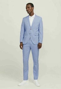 Light blue suit made of smooth fabric. Single-breasted jacket with two buttons, notch lapels, and matching trousers. White shirt and white sneakers.