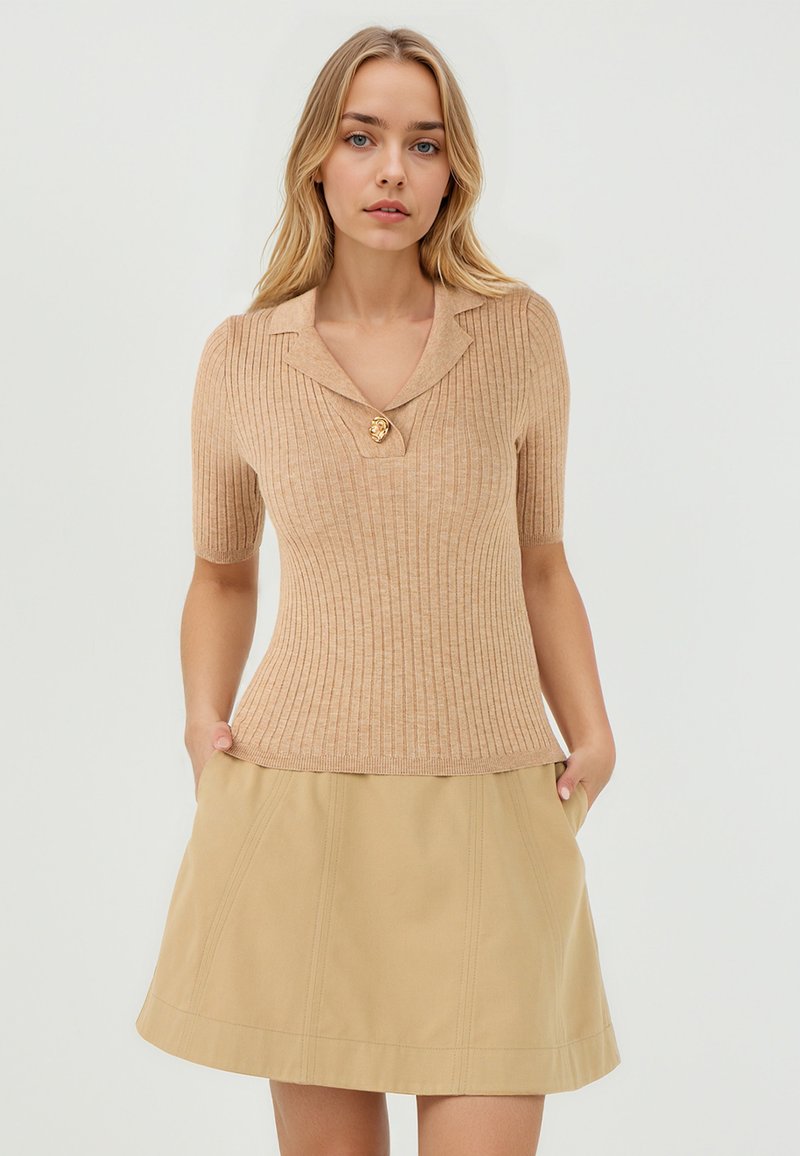 Haut beige à manches courtes et côtelé avec un col en forme de notch et un bouton en forme de lion doré, associé à une jupe A-line beige clair.
