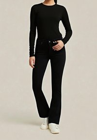 Černý top s dlouhým rukávem v kombinaci s černými džíny s vysokým pasem, které mají přiléhavý střih, mírné rozšíření dole a bílé tenisky.