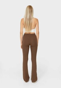 Pantalons évasés marron à côtes avec une taille haute, fabriqués dans un matériau extensible, se terminant au-dessus des chaussures.