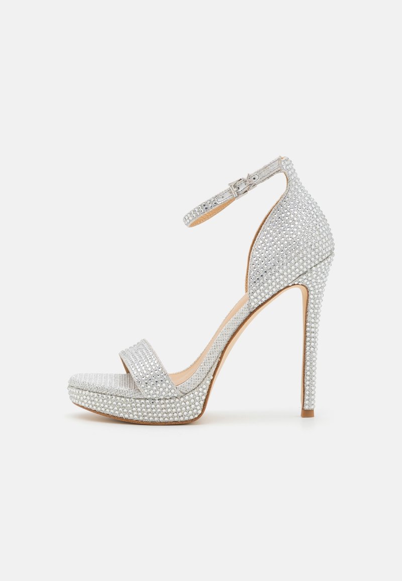 Sandale argentée à talon haut avec ornements en strass, bout ouvert, bride à la cheville et talon aiguille. Texture lisse avec une finition brillante.