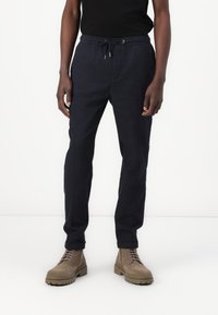 Pantalon de jogging bleu marine en tissu léger. Il dispose d'une taille élastique avec cordon de serrage, de poches latérales et de jambes fuselées.