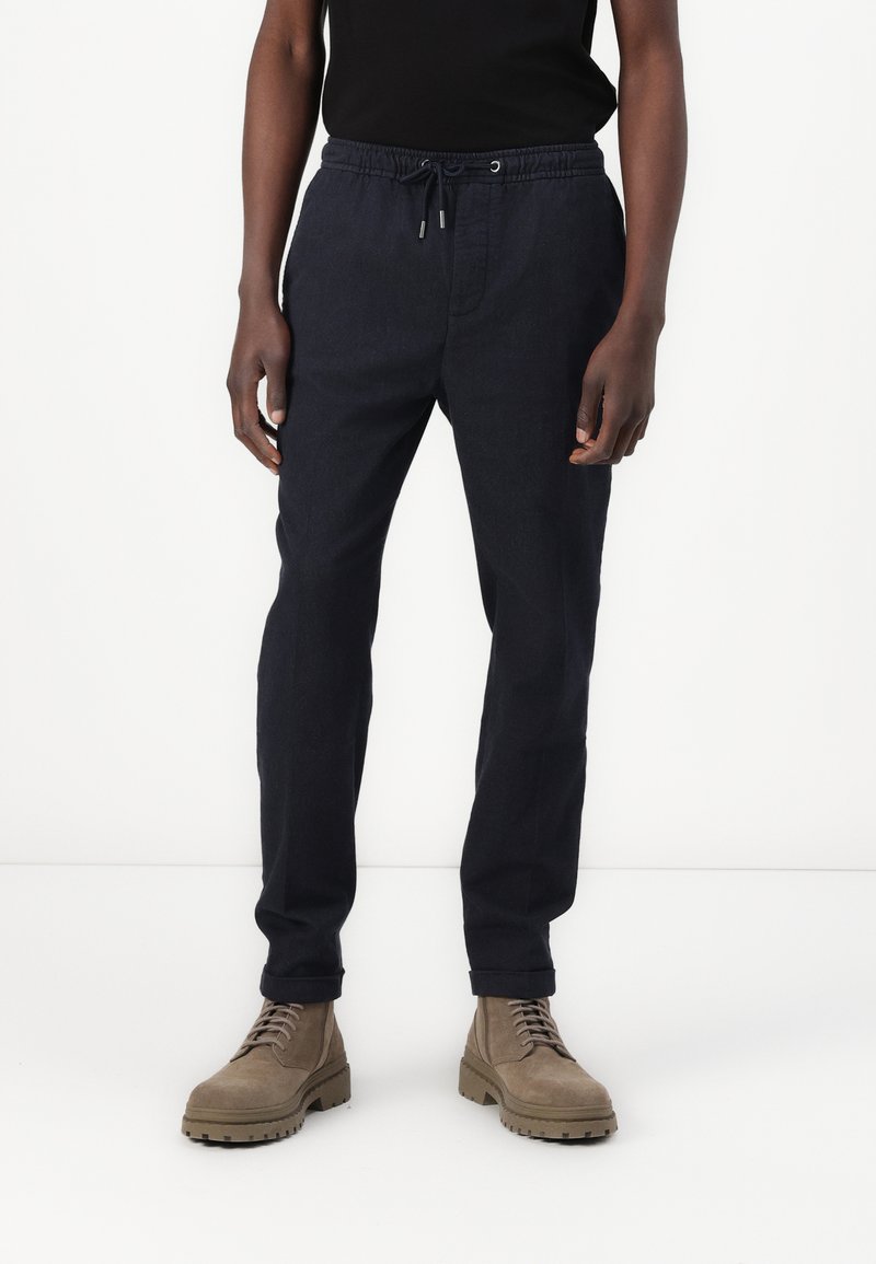 Pantalon de jogging bleu marine en tissu léger. Il dispose d'une taille élastique avec cordon de serrage, de poches latérales et de jambes fuselées.