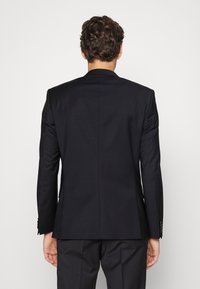 Giacca da abito nera, design a bottoni singoli, tessuto liscio, rever a punta, schiena con ventagli, e polsini con bottoni.