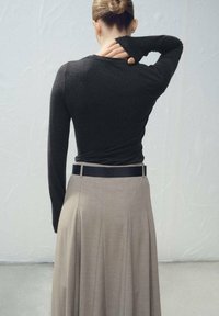 Temno dolg rokav z oprijetim krojem, kombiniran z visokim pasom bež gubanega krila. Gladek teksturen, minimalističen dizajn.