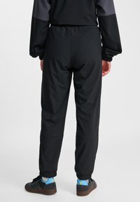 Svarta träningsbyxor med elastisk midja och manschetterade anklar, tillverkade av ett slätt och lätt material. Bärs med svarta och blå sneakers.