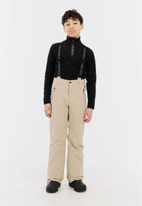 Beige sneeuwbroeken met verstelbare zwarte banden, ritszakken en een relaxte pasvorm. Gepaard met een zwarte rits-top. Zwarte schoenen maken de outfit compleet.