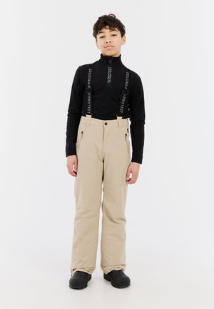 Beige sneeuwbroeken met verstelbare zwarte banden, ritszakken en een relaxte pasvorm. Gepaard met een zwarte rits-top. Zwarte schoenen maken de outfit compleet.