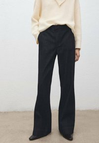 Pantalon en denim taille haute à jambes larges, de teinte foncée, associé à un pull en maille crème texturé, avec une coupe décontractée et des coutures droites.