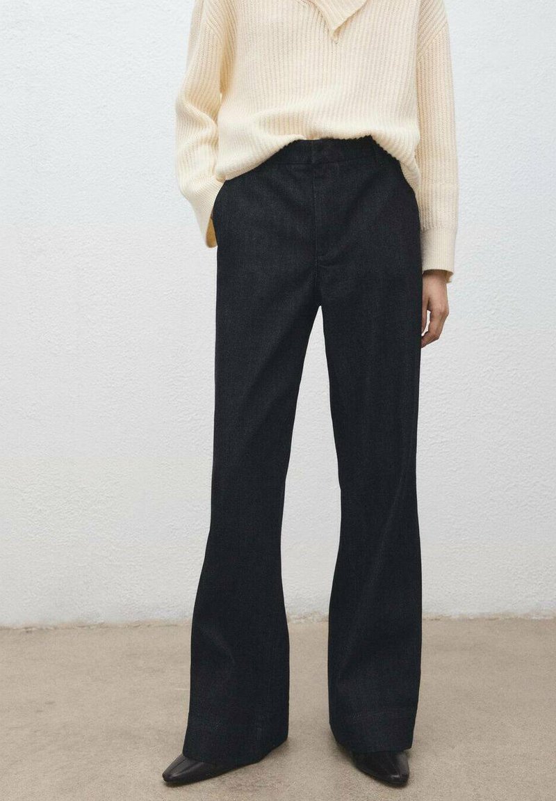 Pantalon en denim taille haute à jambes larges, de teinte foncée, associé à un pull en maille crème texturé, avec une coupe décontractée et des coutures droites.