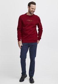 Bordo krūšturis ar apaļu kakla izgriezumu un dekoratīvu tekstu; kombinēts ar tumši ziliem biksēm un melniem apaviem. Gluda tekstūra un ikdienišķa piegriezne.