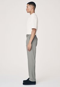 Camicia beige chiaro a maniche corte, pantaloni grigi a gamba dritta e scarpe nere. Tessuto liscio, vestibilità slim e design semplice. Vista di profilo laterale.