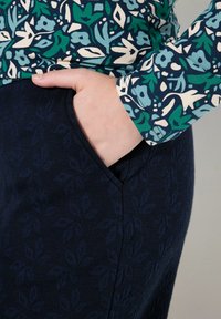 Kukallinen pitkähihainen paita, jossa on sinisiä, vihreitä ja kermaisia kuvioita, yhdistettynä tummansiniseen hameeseen, jossa on teksturoitu lehtikuvio ja sivutasku.