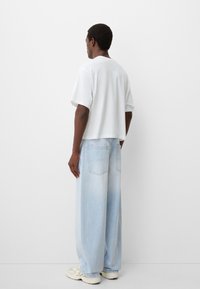 Weißes, kurzes T-Shirt mit kurzen Ärmeln, kombiniert mit hellblauen Jeans im weiten Schnitt, die zwei Gesäßtaschen und eine helle Waschung aufweisen.