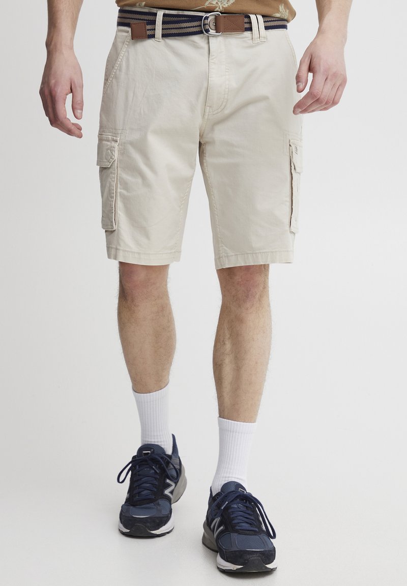 Beige cargo shorts yang terbuat dari bahan ringan dengan dua kantong samping, dipadukan dengan sepatu olahraga navy dan kaus kaki crew putih.