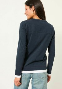 Marineblaue Langarmbluse mit lockerer Passform, runder Ausschnitt, subtiler Textur und kontrastierenden weißen Bündchen, kombiniert mit hellen Jeans.