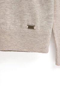 Beiger Pullover mit geripptem Saum und Bündchen. Ein kleines braunes Etikett mit "POLO CLUB" ist nahe dem Saum angebracht. Weiches, strukturiertes Material.