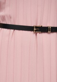 Dettaglio di un vestito plissettato rosa con una cintura in pelle nera caratterizzata da una fibbia in oro. Texture liscia con pieghe strutturate.