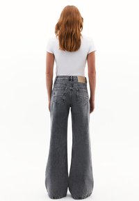Jeans de pierna ancha con un lavado gris desvanecido, que presentan bolsillos traseros, un parche de cuero en la cinturilla y una tela de mezclilla texturizada.