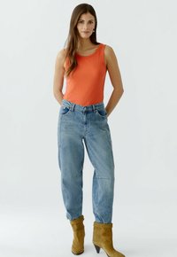 Oranje geribde mouwloze top, hooggepolijste blauwe jeans en tan enkelboots met een spitse neus. Casual outfit met een relaxte pasvorm en zichtbare stiksels.