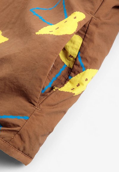 Tissu marron avec un motif d'oiseau jaune et bleu et une ouverture de poche latérale visible sur le matériau.