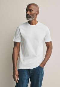 Camiseta blanca de manga corta con escote redondo, hecha de algodón, combinada con jeans de denim azul. La tela parece suave y sin textura.