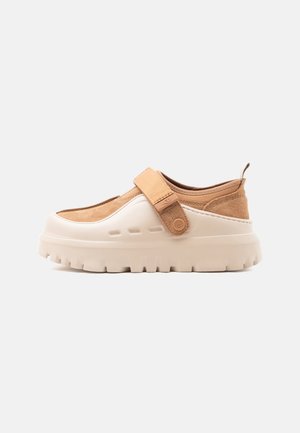 Μπεζ και ταμπά παπούτσι slip-on με χοντρή σόλα με αυλακώσεις και ρυθμιζόμενο λουράκι στο πάνω μέρος, κατασκευασμένο από σουέτ και καουτσούκ.