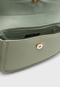 Borsa a tracolla in pelle verde con chiusura a scatto. L'interno include una tasca con zip, rivestita in morbido tessuto. Finiture in oro.