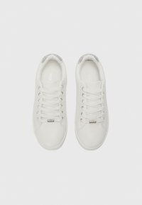 White leather sneakers with silver glitter accents on the heel, round toe, and lace-up front. Ventilation holes on the sides.