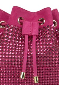 Bolso rosa con textura de ante y brillante strass. Presenta ojales dorados y un cierre con cordón, destacando su diseño distintivo.