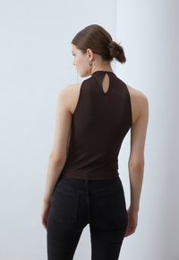 Top bej fără mâneci cu un gât înalt și o deschidere în formă de cheie pe spate, realizat dintr-un material neted și elastic. Asociat cu o pereche de blugi negri.