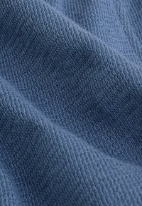 Textil in tiefblau mit einer strukturierten, gewebten Oberfläche. Der Stoff zeigt ein feines Muster von erhabenen Linien, das auf ein weiches, aber dennoch strapazierfähiges Material hinweist.