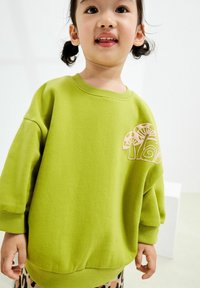 Zielony bawełniany sweatshirt z okrągłym dekoltem, opuszczonymi ramionami oraz dekoracyjnym haftem grzyba w jasnoróżowym kolorze.
