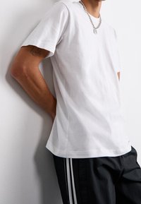 Bílá bavlněná tričko s kr átkým rukávem, kulatým výstřihem a volným střihem, spárované s černými elastickými kalhotami s dvěma bílými pruhy.