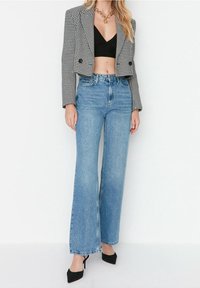 Blazer de espiga recortado sobre una camiseta negra, combinado con jeans de tiro alto y pierna ancha azul y tacones negros; presenta un diseño clásico.
