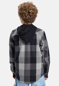 Kostkovaná flanelová košile v šedé a černé barvě s černou kapucí. Má manžety na knoflíky a zakulacený lem. Texturovaná látka s jemným povrchem.
