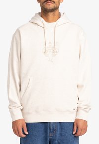 Beige pullover hoodie i et blødt, struktureret stof med en front kangaroo lomme, snøre i hætten og en diskret trykt grafik på brystet.