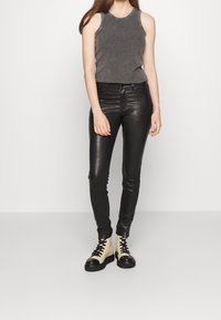 Jeans skinny in pelle nera, top senza maniche grigio e stivaletti alla caviglia bicolore con cappuccio nero e parte superiore bianca. Texture liscia, design aderente.