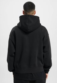 Sort hættetrøje med ribbede manchetter og kant. Blødt stof, løs pasform, minimalistisk design og en stor lomme på ryggen.