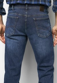 Donkerblauwe spijkerbroek van denim met een gladde textuur, voorzien van twee achterzakken met subtiele stikseldetails en een bruin leren label op de taille.