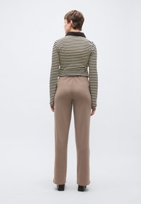 Top de manga comprida às riscas em preto e creme com gola, combinado com calças castanhas ajustadas. Textura suave e design ajustado.