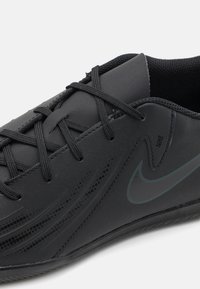 Fekete sportcipő szintetikus felsőrésszel, texturált felülettel, lapos fűzőkkel és diszkrét Nike logóval. Alacsony profilú kialakítással rendelkezik.