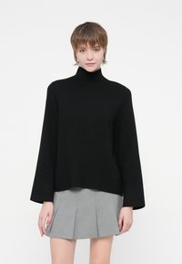 Musta poolpikkade varrukatega turtleneck-sviiter, millel on lõdva lõikega ja mis on valmistatud pehmest materjalist, koos halli volditud seelikuga.