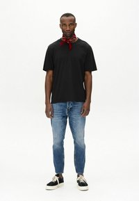 Tricou negru cu mânecă scurtă, blugi albaștri și adidași negri cu talpă albă. O bentiță roșie legată la gât adaugă detalii ținutei.
