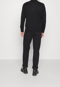 Maglione nero lavorato a maglia con maniche lunghe, abbinato a pantaloni neri. I pantaloni hanno le estremità arrotolate e sono indossati con stivaletti neri.