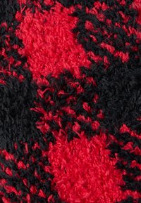 Υφασμα με υφή που παρουσιάζει ένα μοτίβο σε μαύρο και κόκκινο χρώμα, με αφράτες ίνες που δημιουργούν μια απαλή, βελούδινη επιφάνεια. Διακρίνονται έντονα αντιθετικά χρώματα και μοτίβα.
