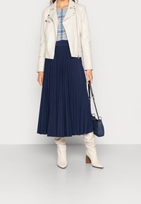 Biała skórzana kurtka motocyklowa, niebieska koszula w kratę, plisowana granatowa spódnica, kremowe kozaki do kolan oraz mała dżinsowa torebka.