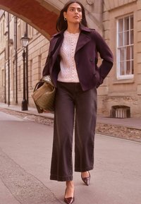 Jachetă visinie cu două rânduri de nasturi, pulover cremos din lână împletită, pantaloni negri cu picioare largi și pantofi cu vârful ascuțit în nuanță burgundy. Geantă țesută verde inclusă.